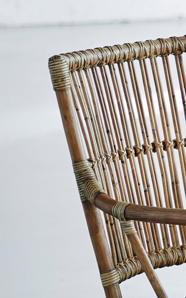 This is a close-up image of Piano Dining Chair in antique rattan. Detail of the vertical rattan spindle backrest and wrapped joints.