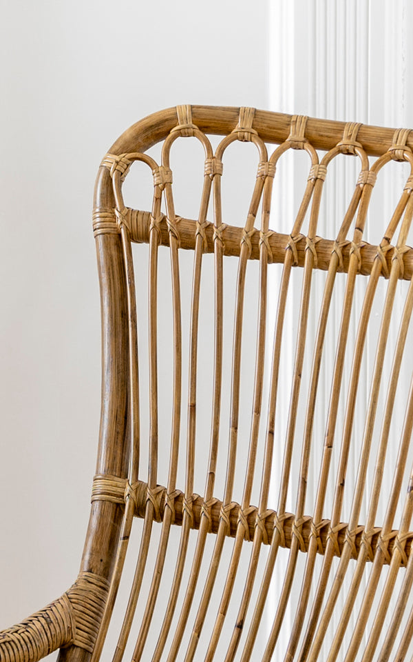 This is a close-up image of Monet Rocking Chair in antique rattan. Detail of the looped arch backrest and vertical rattan rod construction.