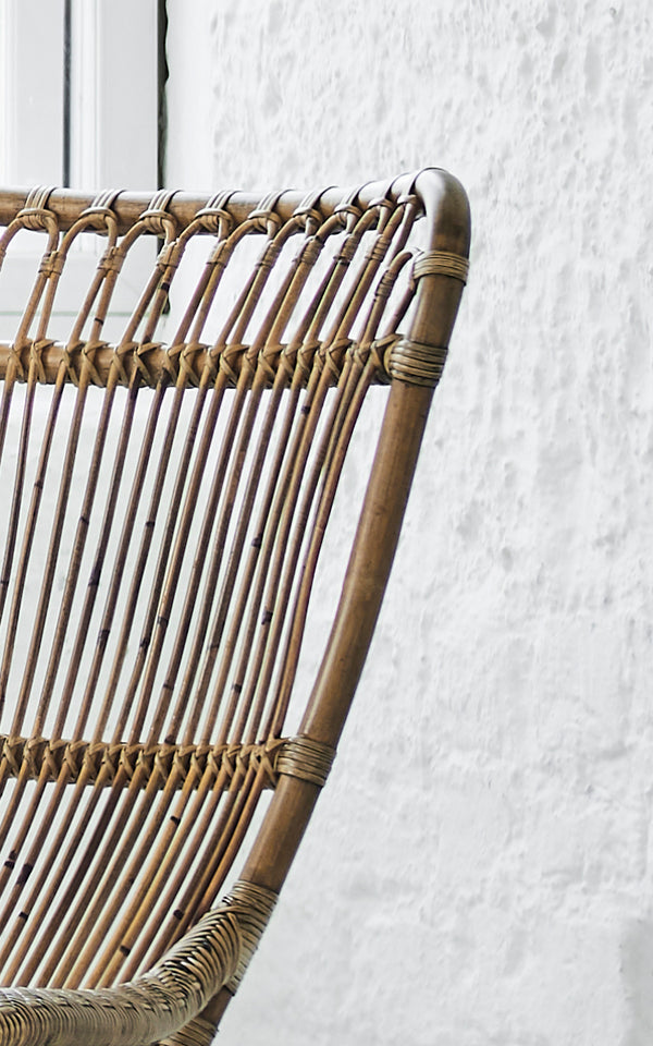 This is a close-up image of Monet Lounge Chair in antique rattan. Detail of the looped arch backrest with vertical rods and woven seat.