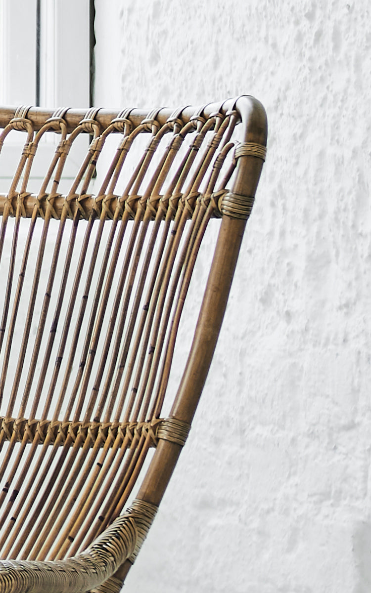 This is a close-up image of Monet Lounge Chair in antique rattan. Detail of the looped arch backrest with vertical rods and woven seat.