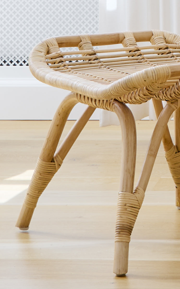 This is a close-up image of Monet Footstool in natural rattan. Detail of the flat woven seat and wrapped rattan joints on the legs.