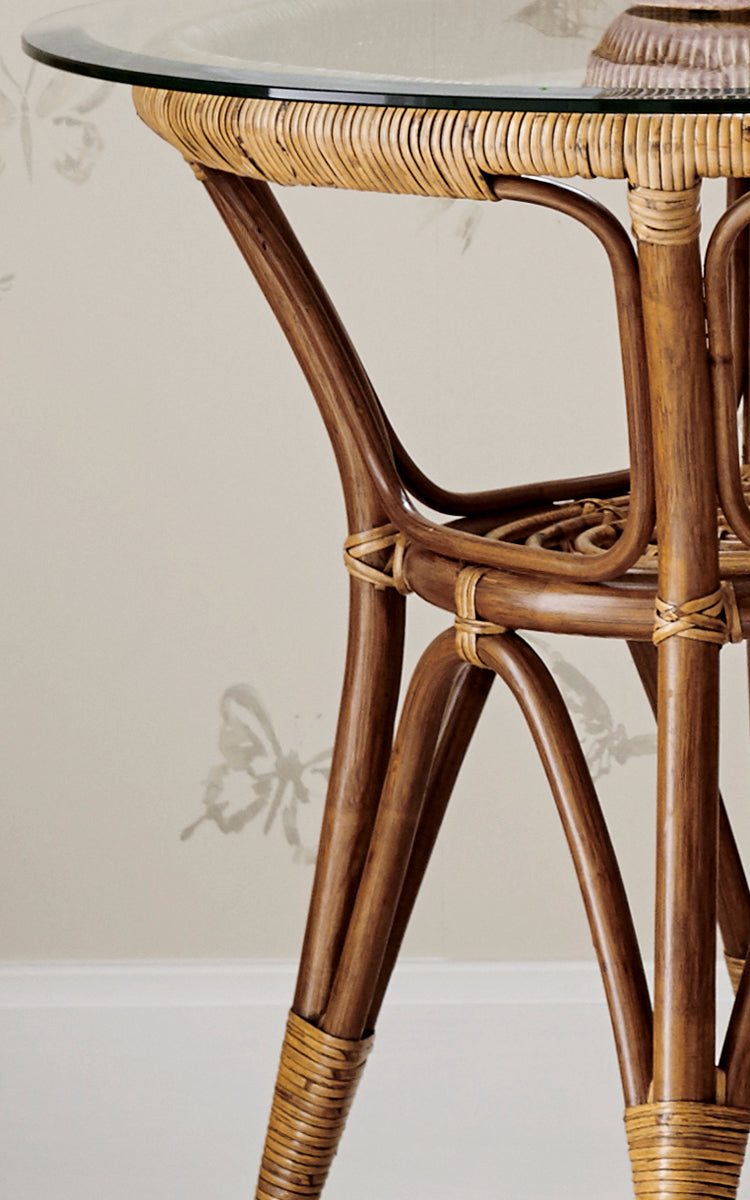 This is a close-up image of Tony Side Table in antique rattan. Detail of the glass-top edge with wrapped rattan and curved legs.