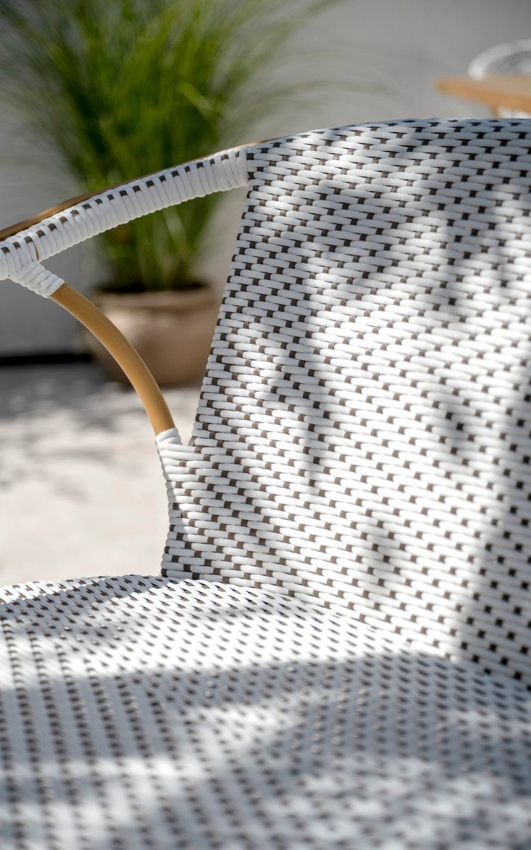 This is a close-up image of Madeleine Exterior Bench in almond aluminium frame white w cappuccino dot artfibre. Woven backrest in dappled light.