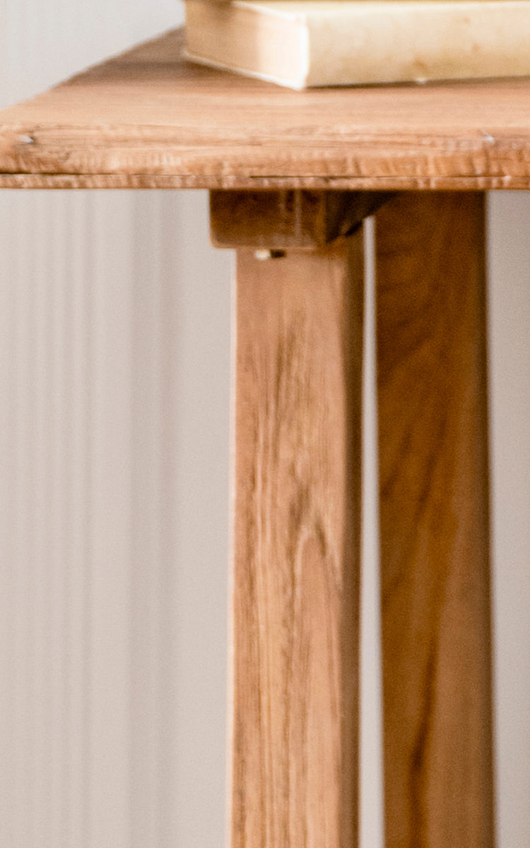 This is a close-up image of Lucas Teak Desk in teak indoor. The solid teak surface edge and angled legs reveal the warm wood grain and sturdy build.