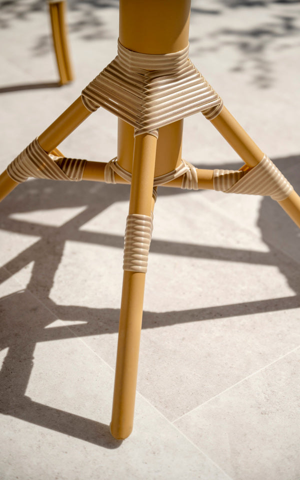 This is a close-up image of Nicole Cáfe Table in almond aluminium frame natural artfibre. Base with wrapped joints on a sunny terrace floor.