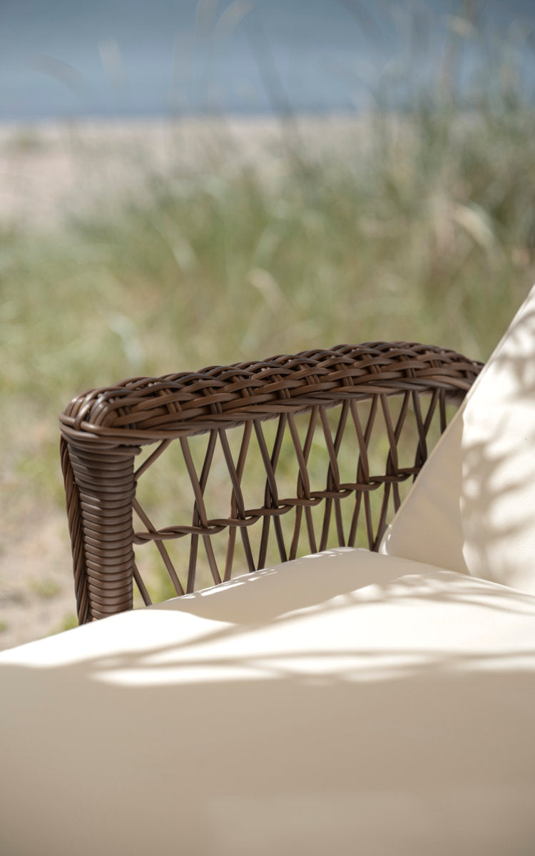 This is a close-up image of Daisy Exterior Sunbed in brown artfibre aluminum. Woven armrest with cream cushion.