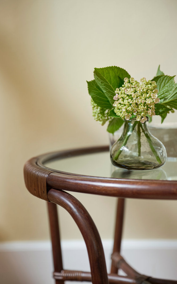 This is a close-up image of Charlottenborg Coffee Table in brown rattan. Glass top and rattan frame with hydrangea vase.