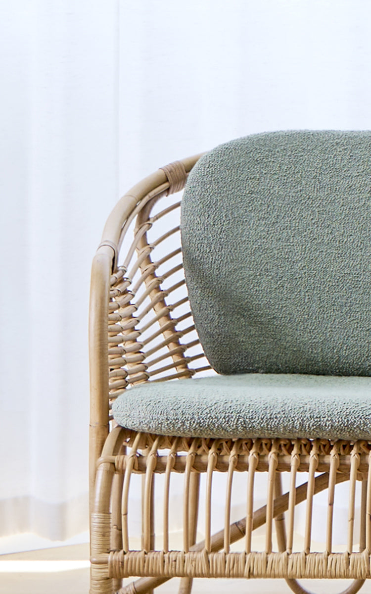 This is a close-up image of Swing Sofa in polished natural rattan. Detail of the curved rattan sofa frame with bouclé seat cushion.