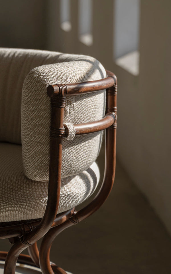 This is a close-up image of Coco Lounge Chair in brown rattan. Bound armrest and soft cushion in daylight.