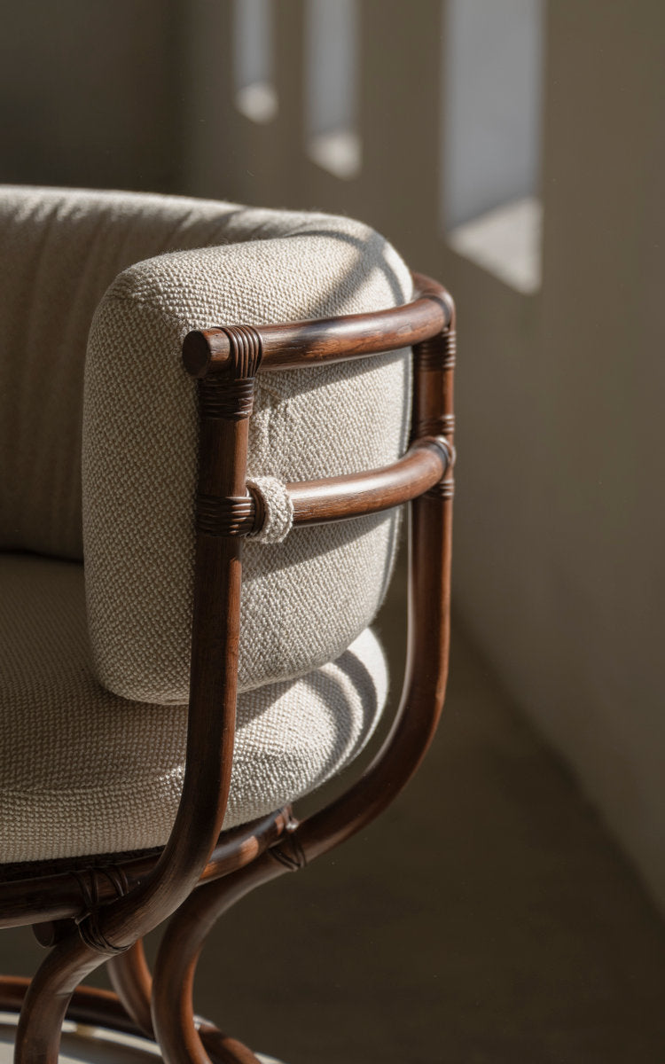 This is a close-up image of Coco Lounge Chair in brown rattan. Bound armrest and soft cushion in daylight.