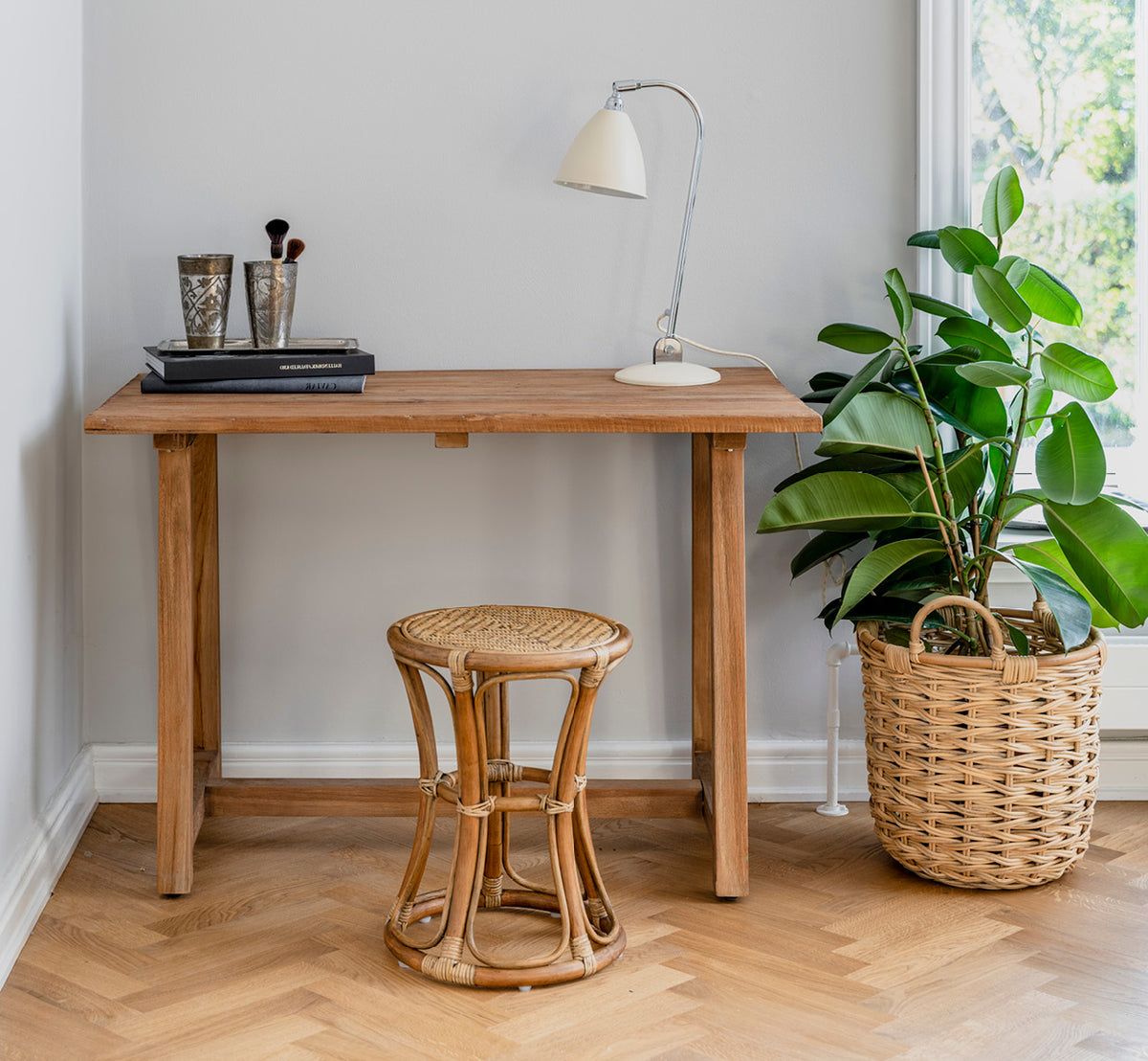 This is a lifestyle image of Bella Stool in antique rattan, in a bright interior with white panelled walls and herringbone parquet.