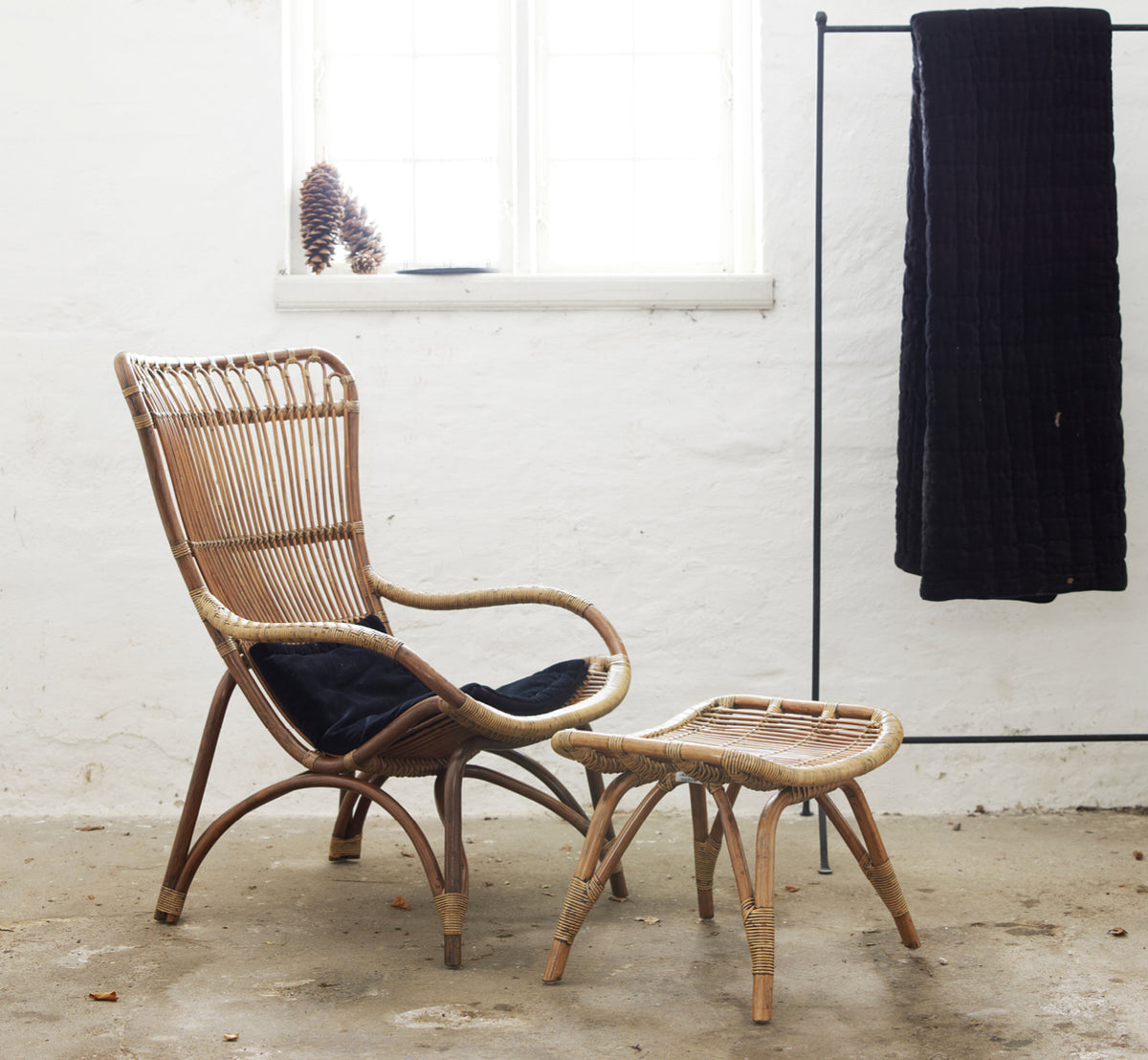 This is a lifestyle image of Monet Lounge Chair in antique rattan. With footstool and side table in a dark rustic barn setting.