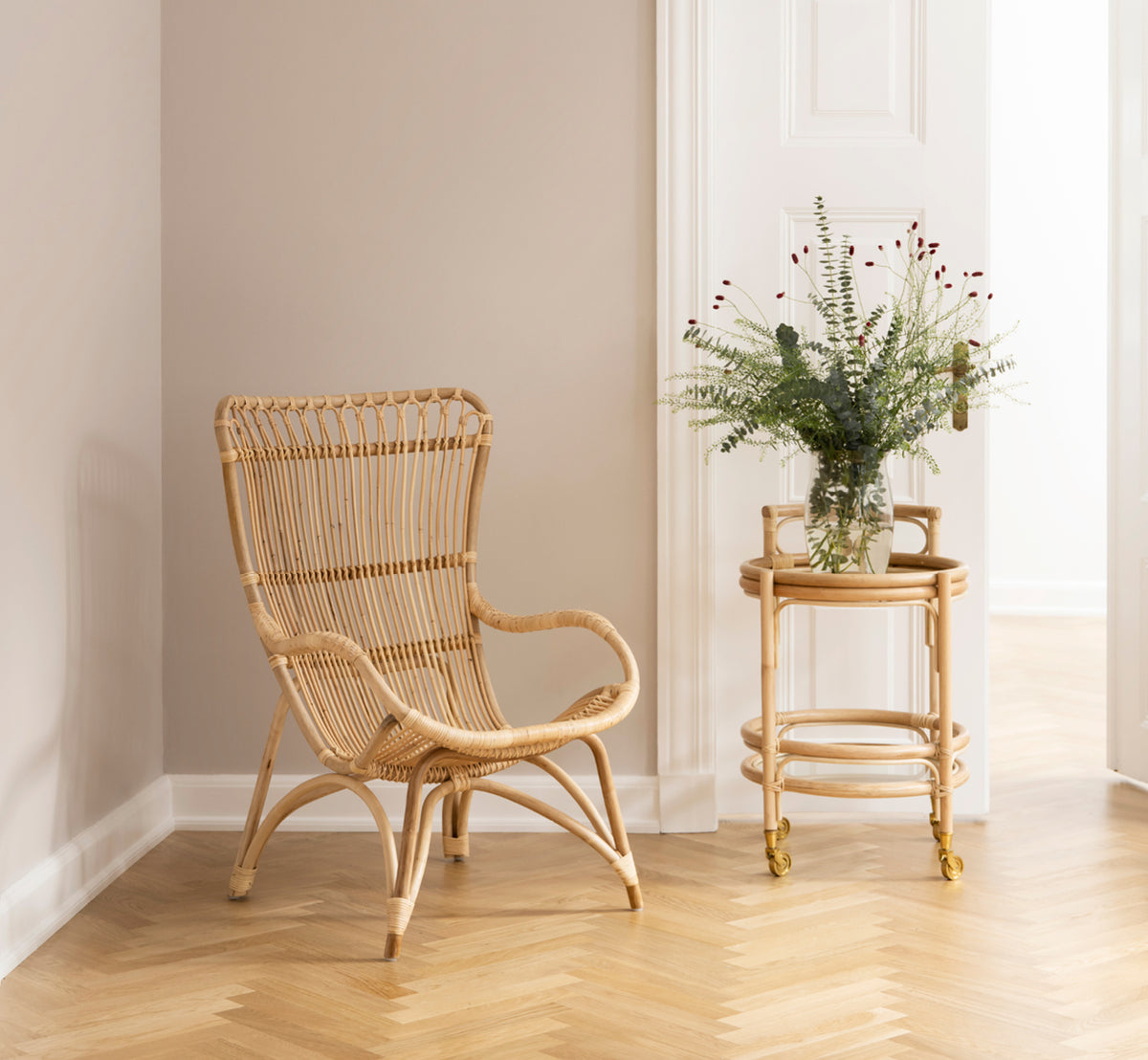 This is a lifestyle image of Monet Lounge Chair in natural rattan. With footstool and side table in a dark rustic barn with candle.