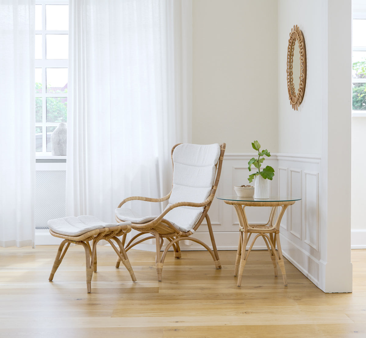 This is a lifestyle image of Monet Footstool in natural rattan. With lounge chair and side table in a bright paneled room.