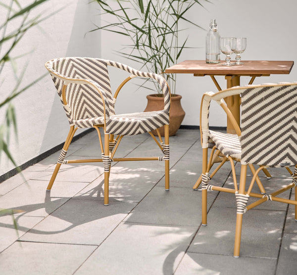 This is a lifestyle image of Madeleine Exterior Dining Chair in almond aluminum frame chevron cappuccino ivory ArtFibre. Sunny terrace with table.