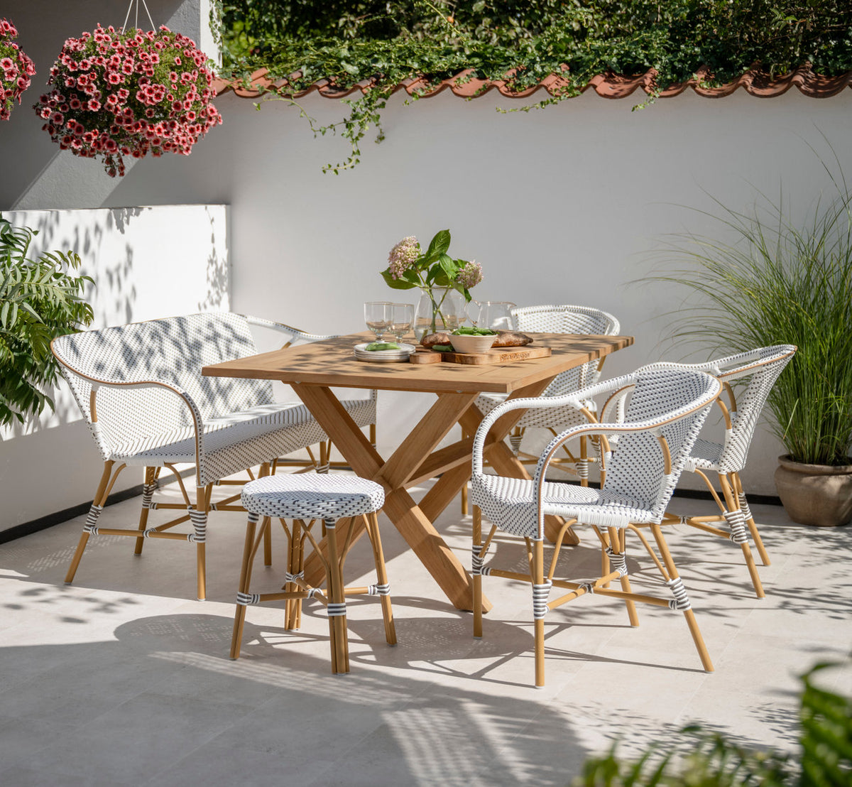 This is a lifestyle image of Madeleine Exterior Dining Chair in almond aluminium frame white w cappuccino dot artfibre. At a teak table on a terrace.