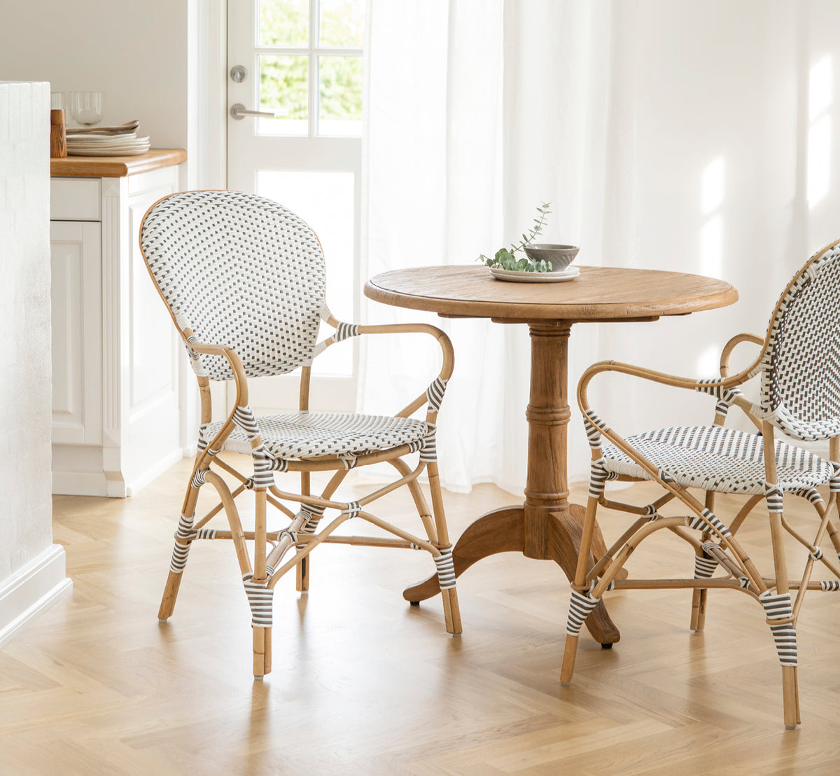 This is a lifestyle image of Isabell Dining Armchair in white w cappuccino dot ArtFibre Skin on Rattan frame, in a bright dining area with large.