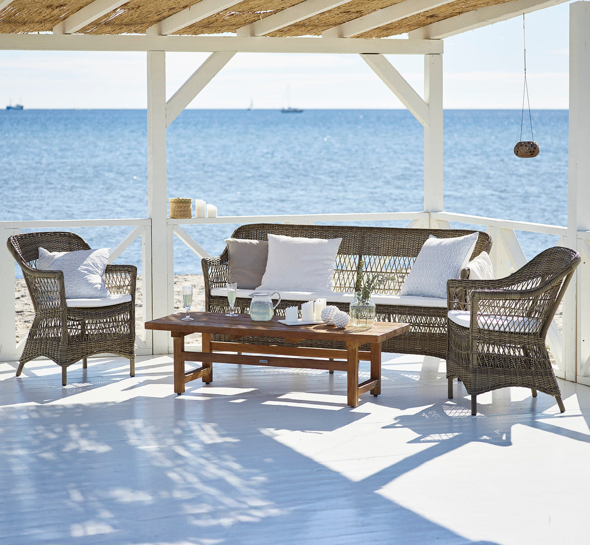 This is a lifestyle image of Charlot Exterior Chair in antique Grey ArtFibre Aluminium, on a sun-drenched coastal terrace with sea views and a white.
