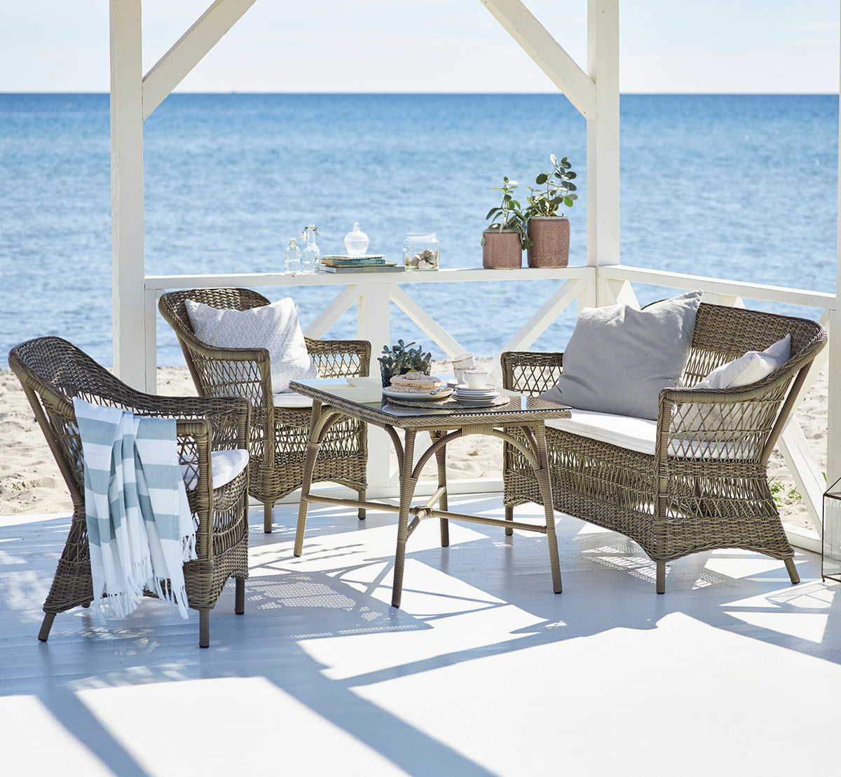 This is a lifestyle image of Charlot Exterior Chair in antique Grey ArtFibre Aluminium, on a sun-drenched coastal terrace with sea views and a white.