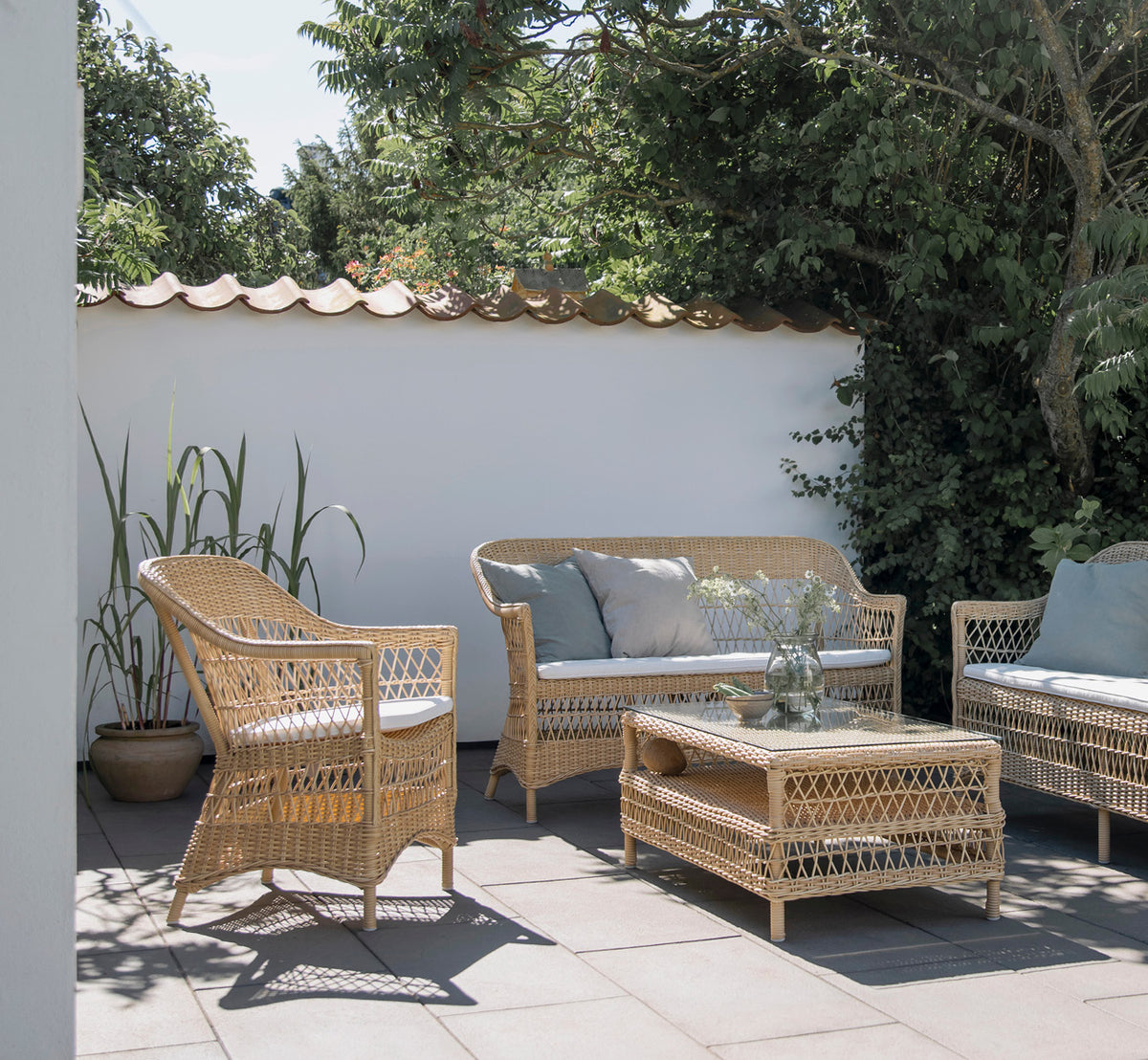 This is a lifestyle image of Charlot Chair in natural ArtFibre Aluminium, on a sun-drenched coastal terrace with sea views and a white pergola.