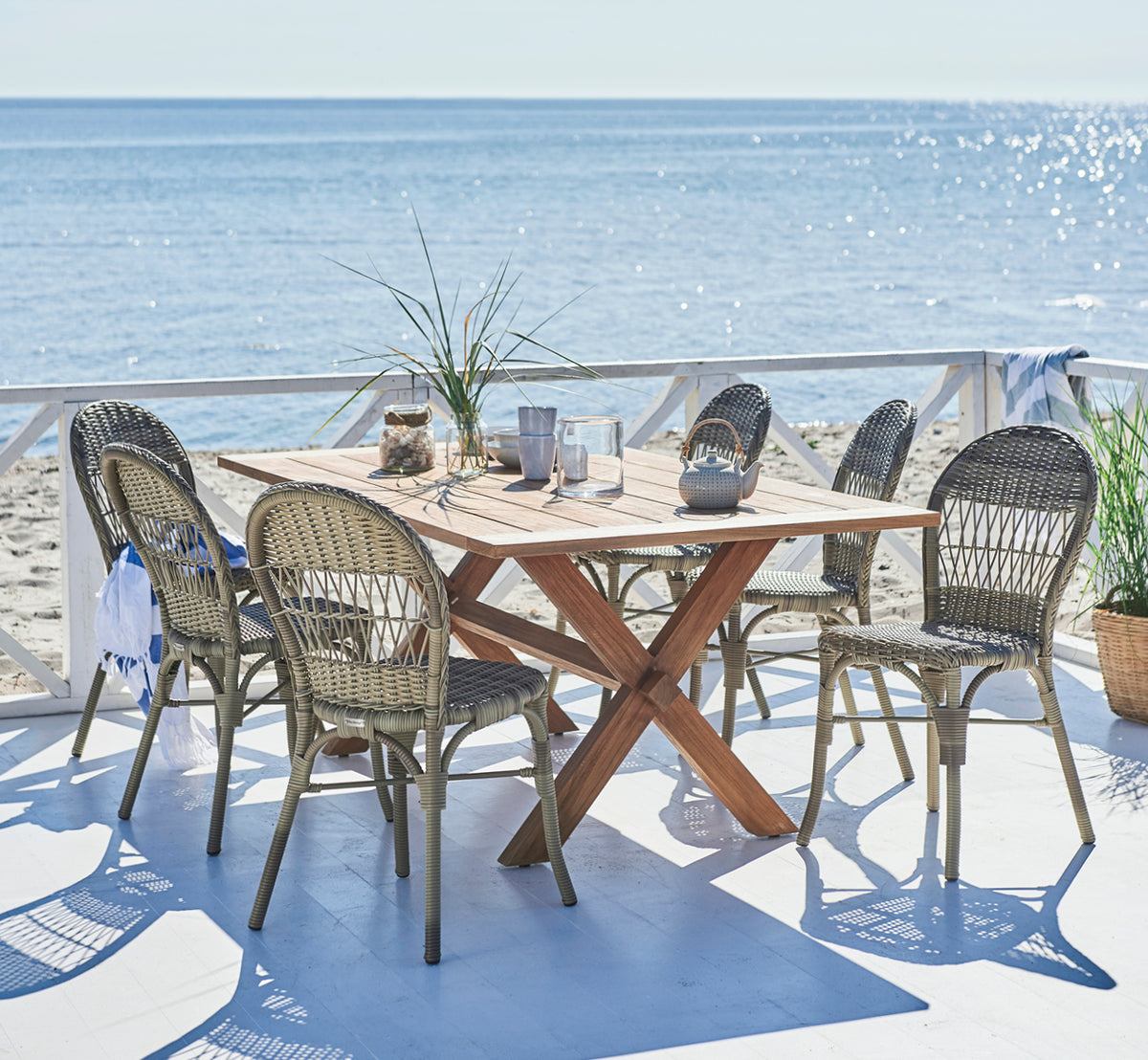 This is a lifestyle image of Ofelia Exterior Chair in antique grey artfibre aluminium. On a beach deck with ocean view and teapot.