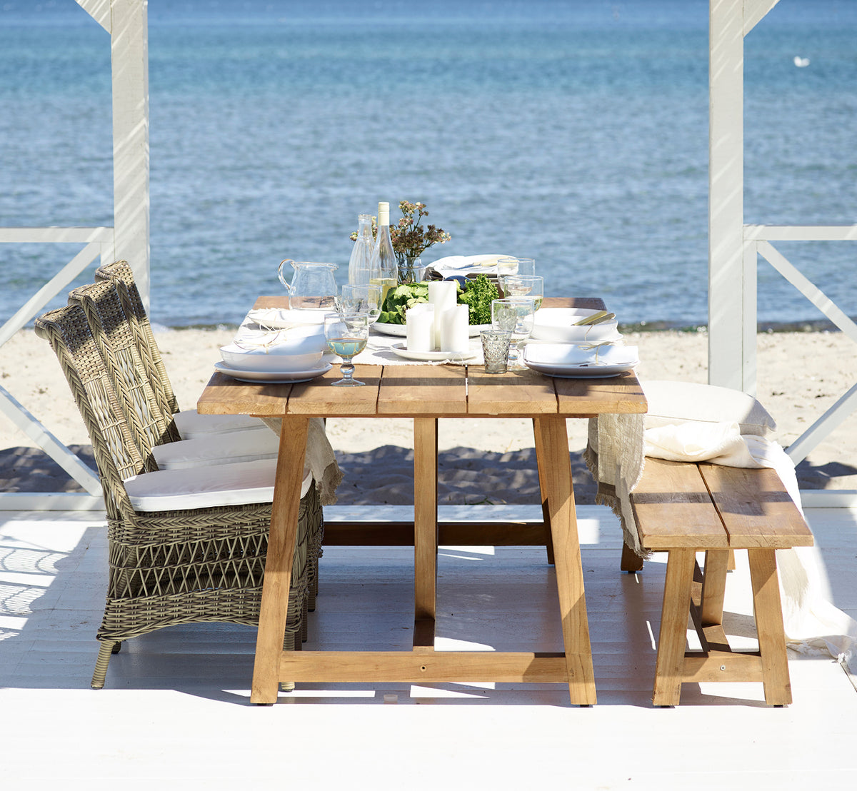 This is a lifestyle image of Marie Exterior Side Chair in antique grey artfibre aluminium. At a teak table on a seaside pavilion.