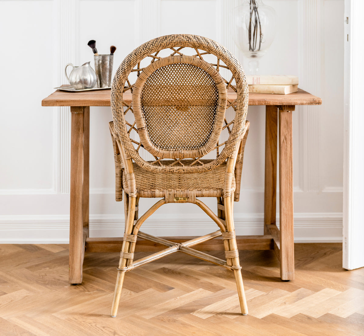 This is a lifestyle image of Lucas Teak Desk in teak indoor. Placed against a gray wall with a teak mirror and pampas grass in a hallway setting.