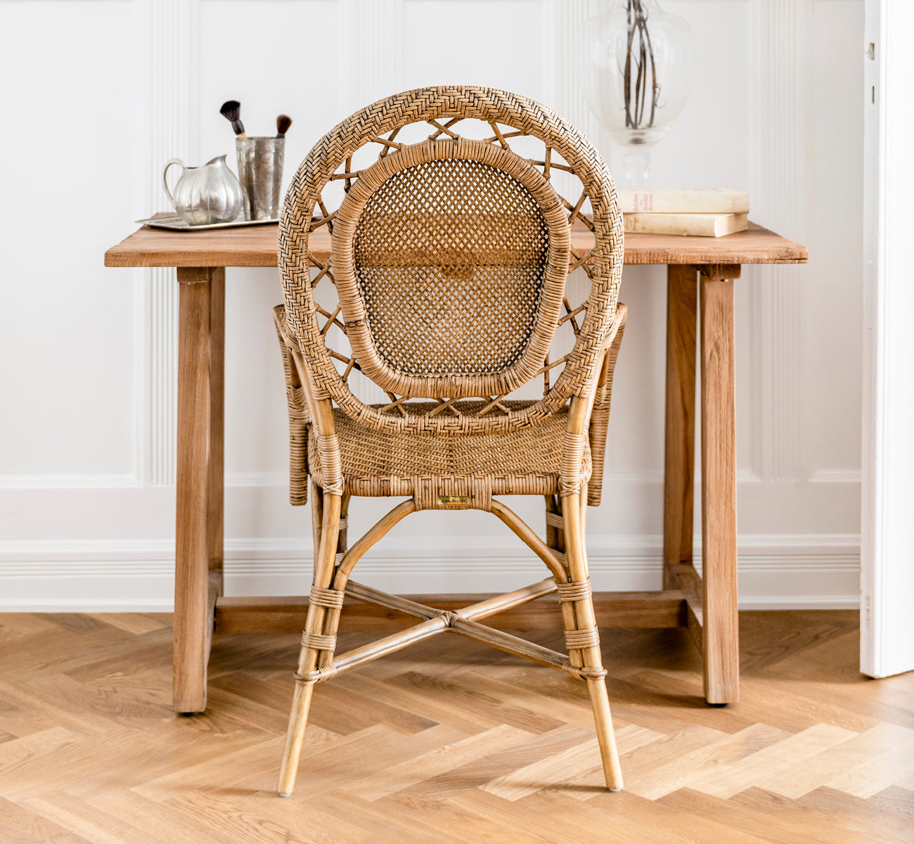 This is a lifestyle image of Lucas Teak Desk in teak indoor. Placed against a gray wall with a teak mirror and pampas grass in a hallway setting.
