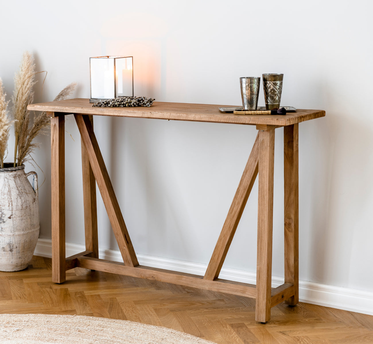 This is a lifestyle image of Lucas Teak Console in teak indoor. Styled with candle holders and pampas grass in a warm setting with a jute rug.