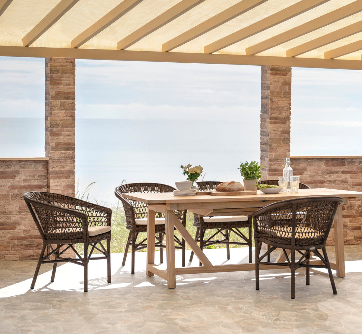 This is a lifestyle image of George Teak Extendable Table 200-280x100 cm in teak outdoor. Set for lunch on a terrace by the sea.