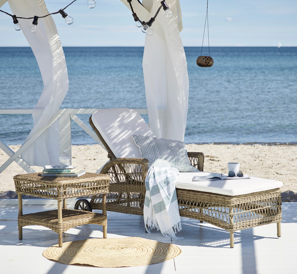 This is a lifestyle image of Susy Side Table in antique Grey ArtFibre Aluminium, on a coastal terrace with sea views, beach grasses and white columns.