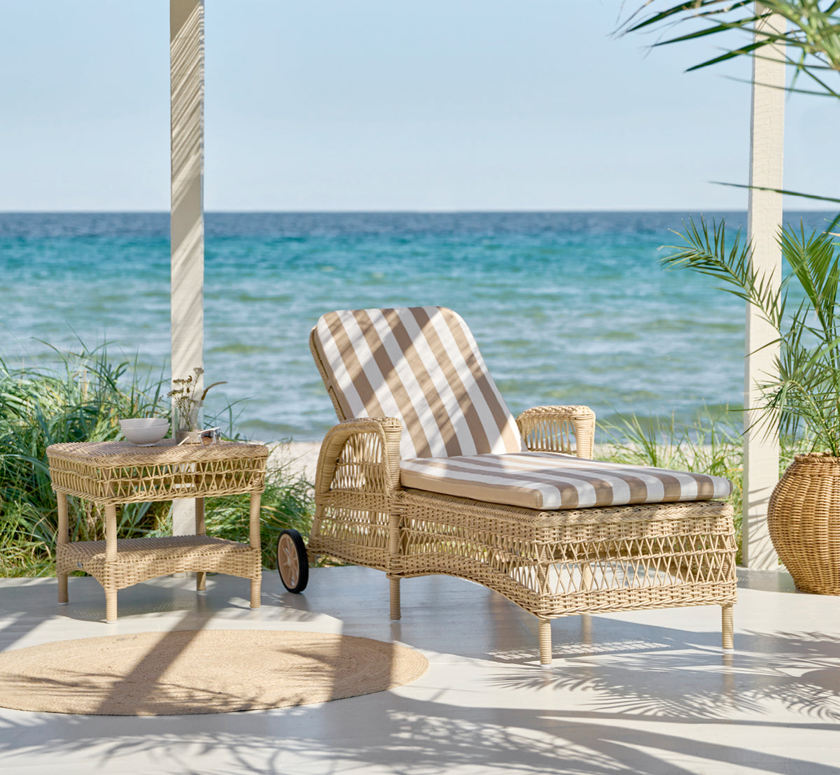 This is a lifestyle image of Daisy Sunbed in natural ArtFibre Aluminium, on a garden terrace surrounded by lush trees and potted plants.