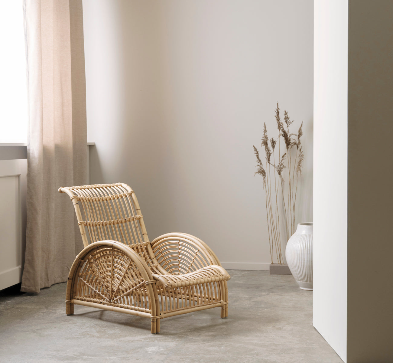 This is a lifestyle image of Paris Lounge Chair in polished natural rattan. Placed on a herringbone parquet floor beside a matching bench.