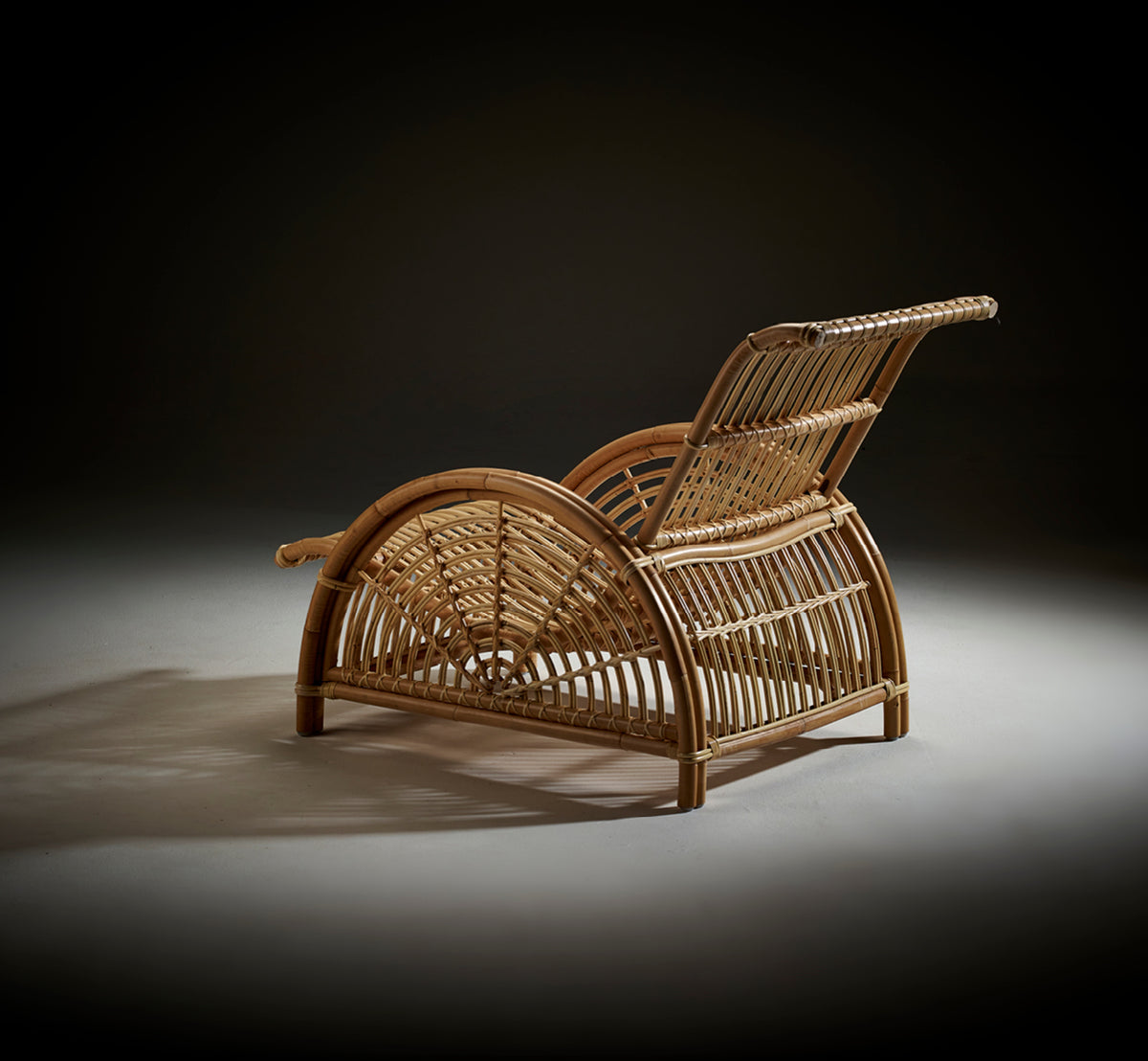 This is a lifestyle image of Paris Lounge Chair in polished natural rattan. Placed on a herringbone parquet floor beside a matching bench.