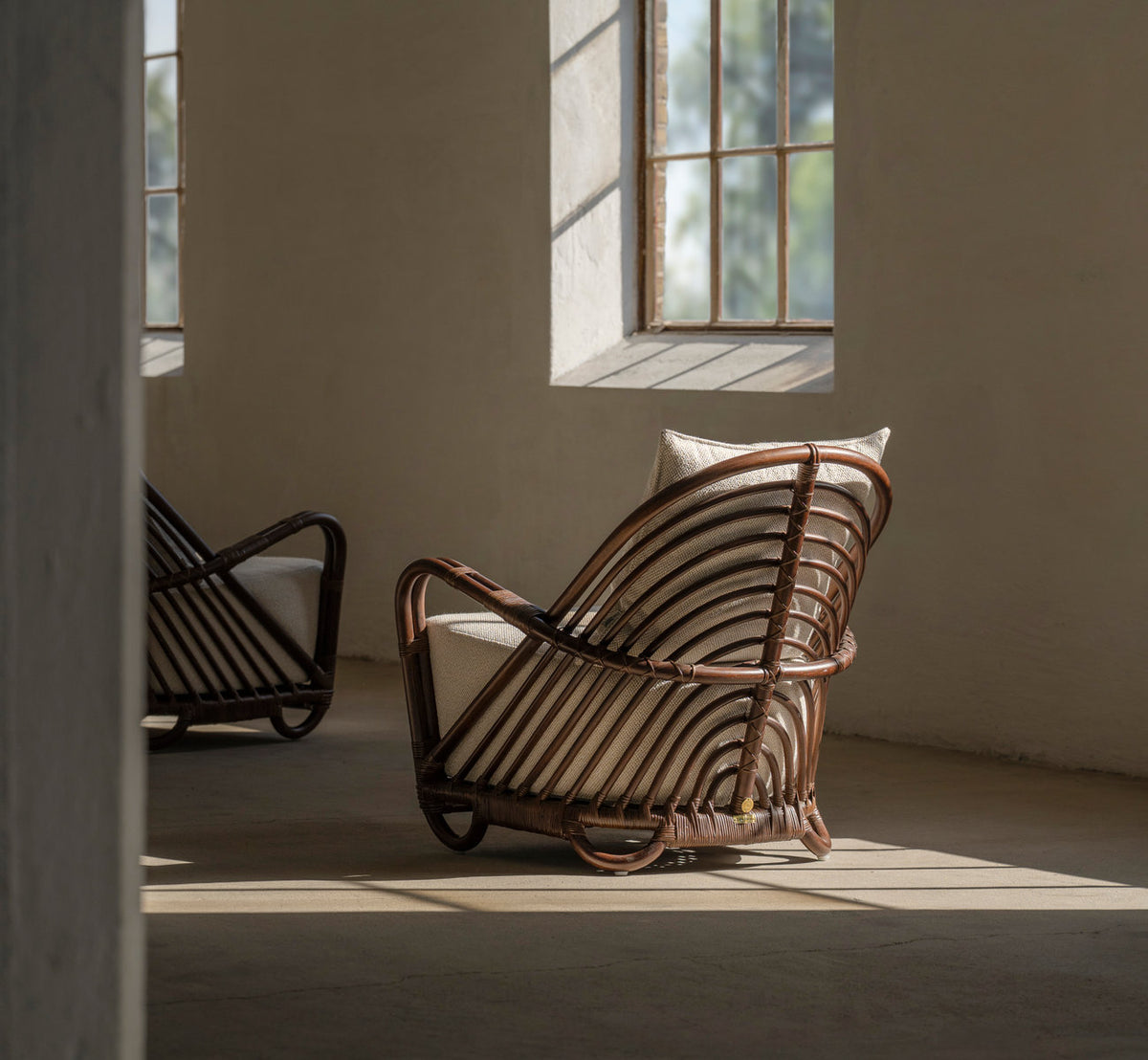 This is a lifestyle image of Charlottenborg Lounge Chair in brown rattan. Pair in soft window light with deep shadows.
