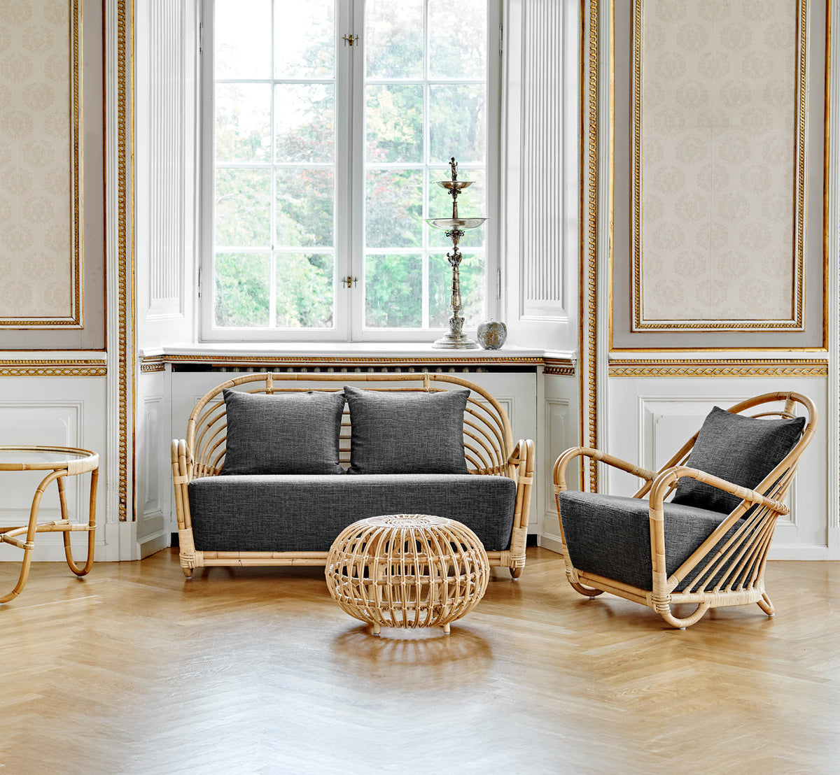 This is a lifestyle image of Charlottenborg Sofa in polished Natural Rattan, in an elegant classical interior with ornate golden mouldings.