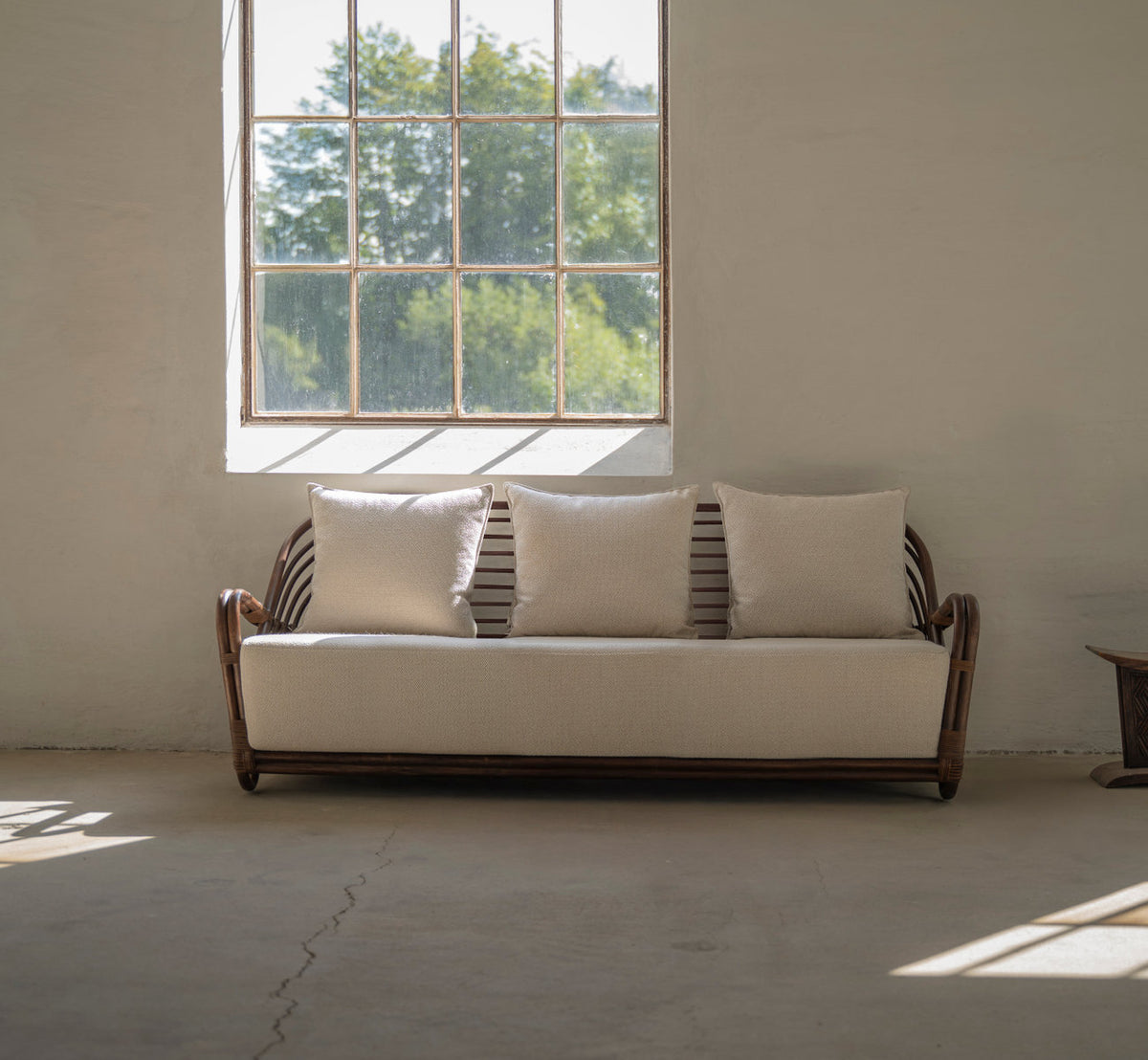 This is a lifestyle image of Charlottenborg 3-Seater Sofa in brown rattan. With linen cushions by a large window.