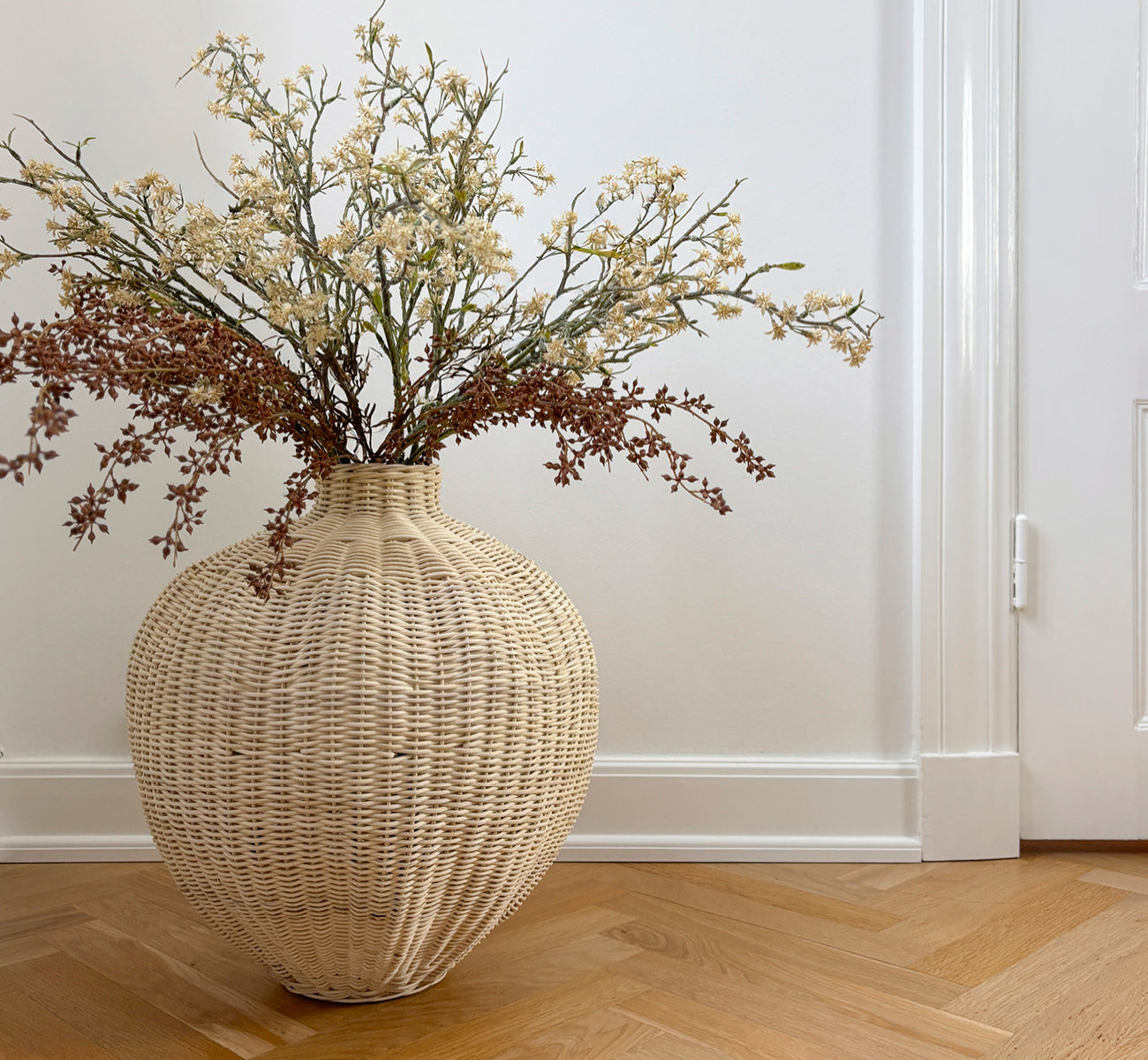 This is a lifestyle image of Flumen Basket in natural core weave iron frame, in a bright white interior with wainscoting, styled with dried flowers.