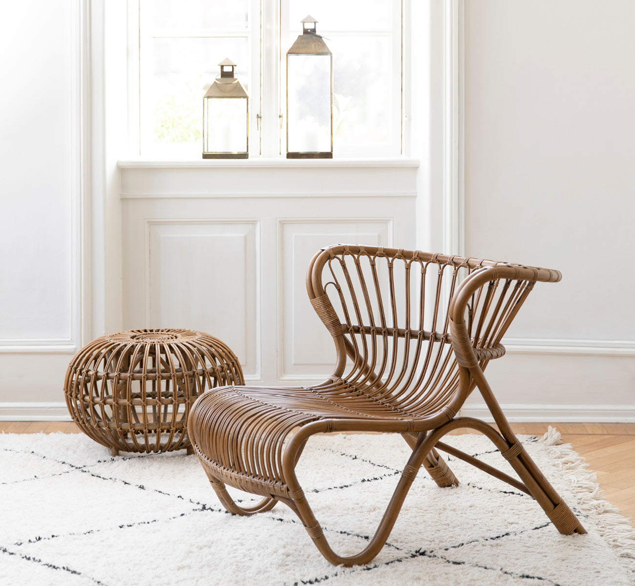 This is a lifestyle image of Ottoman Small in polished antique rattan. Placed in a room with ornate wallpaper and a classical statue.