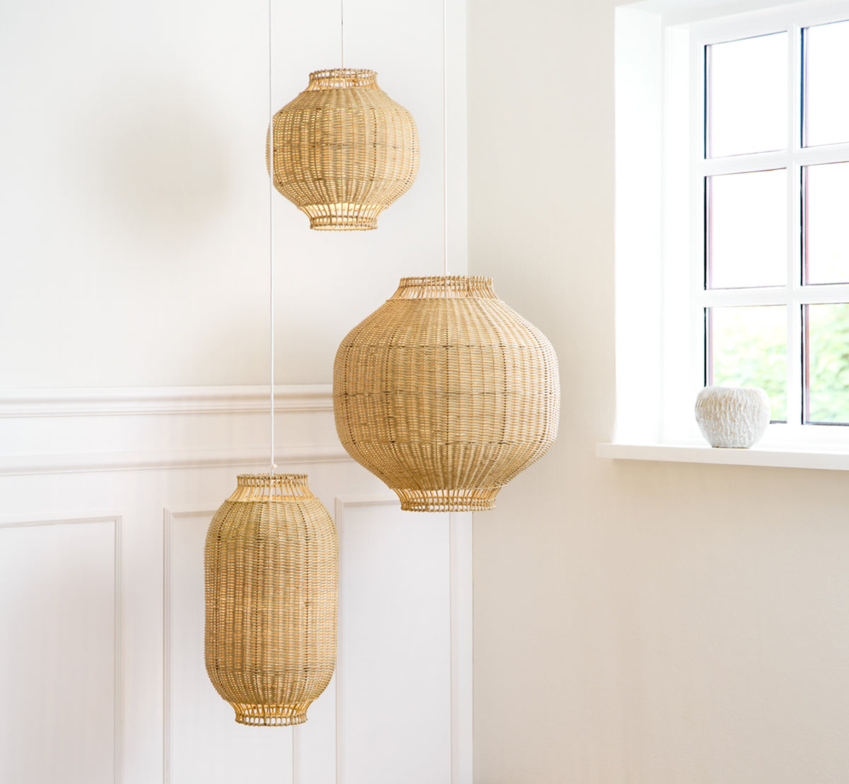 This is a lifestyle image of Tomos Lampshade in natural core weave rattan frame. Hanging with other pendant sizes in a bright paneled room.
