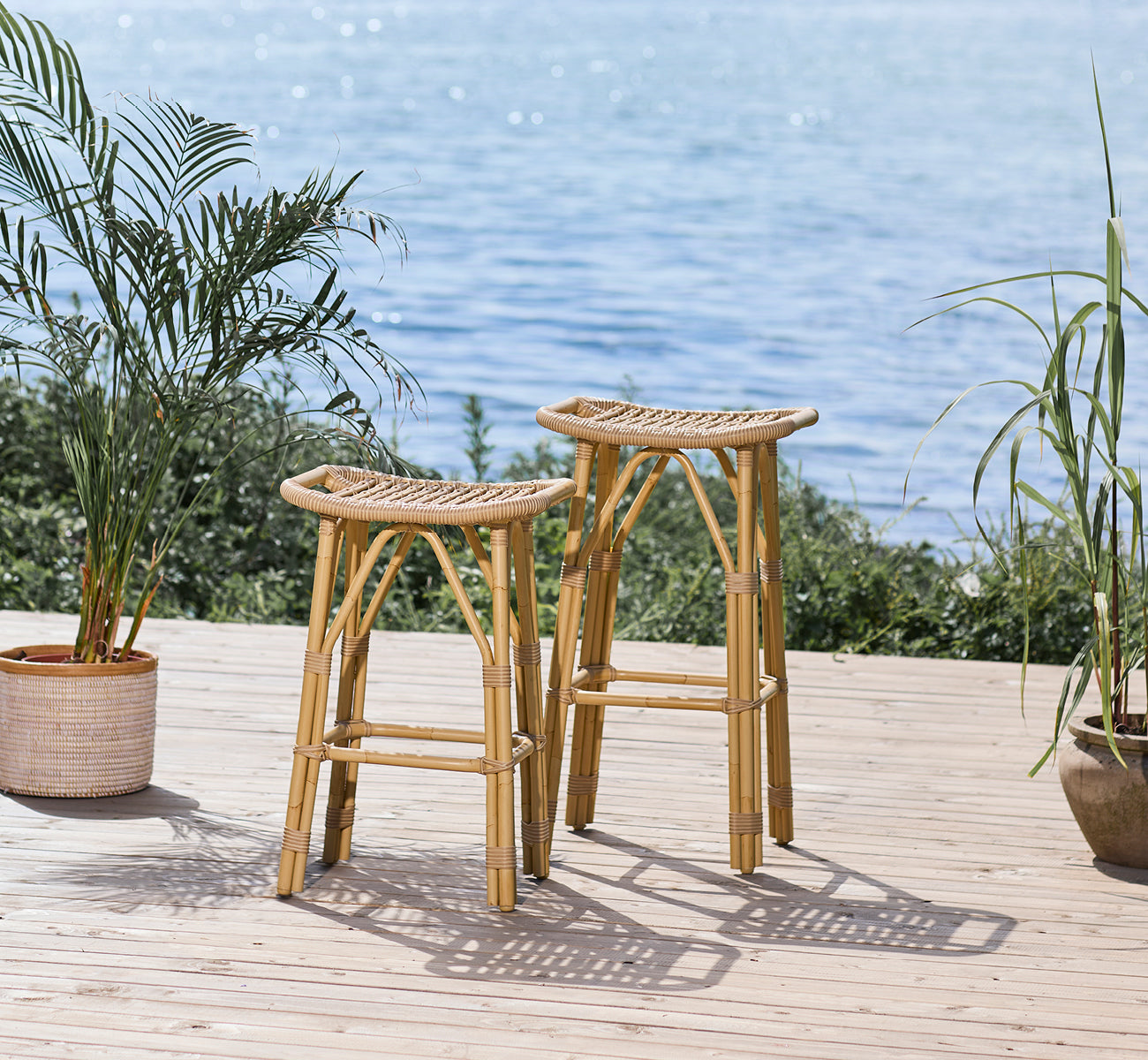 This is a lifestyle image of Salsa Exterior Bar Stool in natural aluminium artfibre. Waterfront deck with palm plants and ocean view.