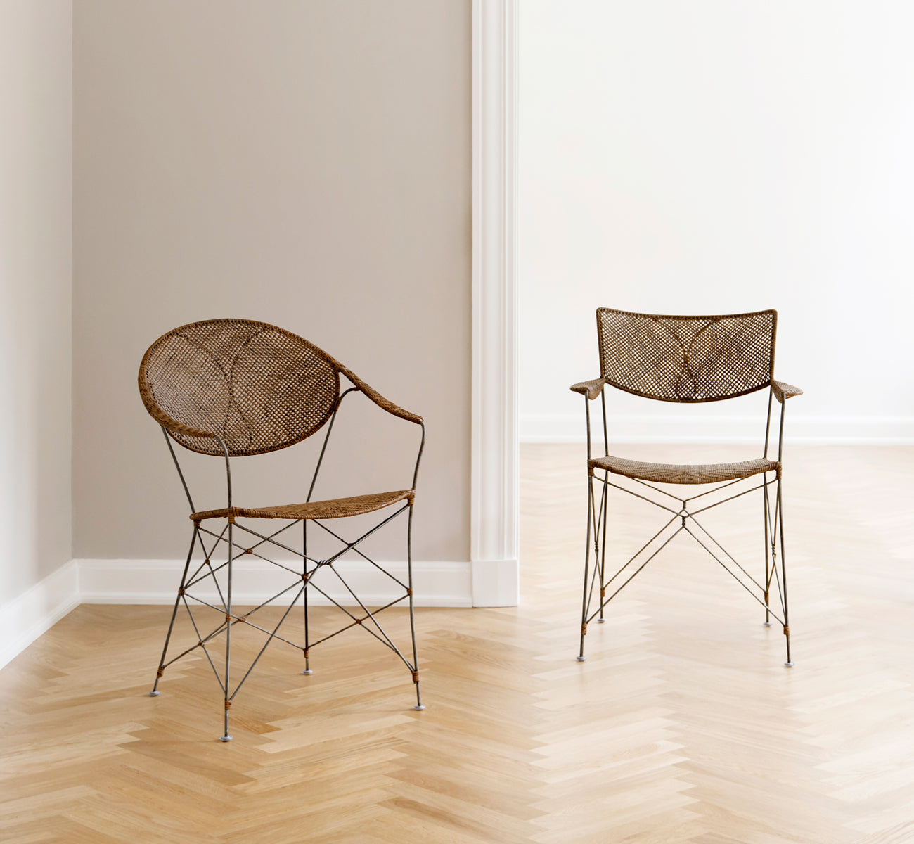 This is a lifestyle image of Rap Dining Chair in hazelnut rattan iron frame, in a bright interior with white panelled walls and herringbone parquet.