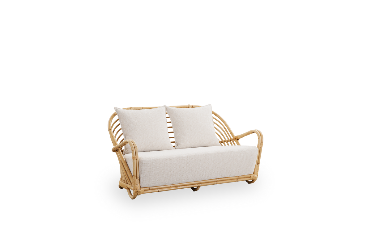 Side view of the Charlottenborg 2-seater Sofa in polished natural rattan, designed by Arne Jacobsen. The sofa features a curved back and armrests integrated into the base, handcrafted from high quality Indonesian rattan.