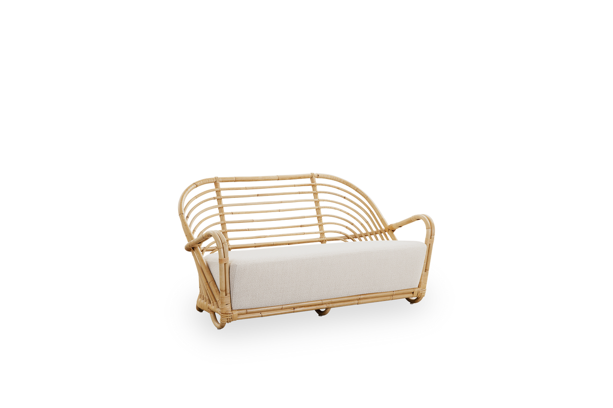 Side view of the Charlottenborg 2-seater Sofa in polished natural rattan, designed by Arne Jacobsen. The sofa features a curved back and armrests integrated into the base, handcrafted from high quality Indonesian rattan.