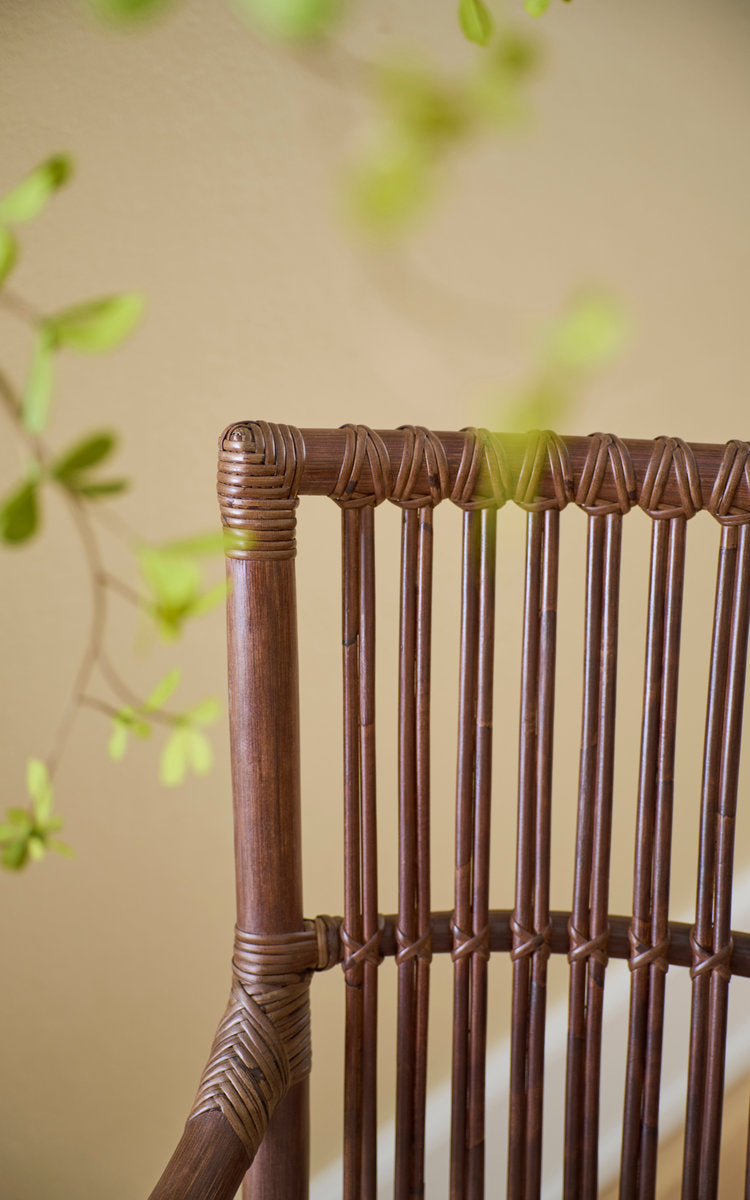 This is a close-up image of Piano Dining Chair in brown rattan. Bound rattan back slats in soft light.