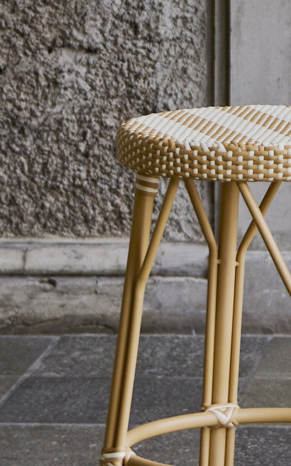 This is a close-up image of Simone Counter Stool in striped honey ivory ArtFibre Skin on Rattan frame. Seat detail against a rough stone wall.
