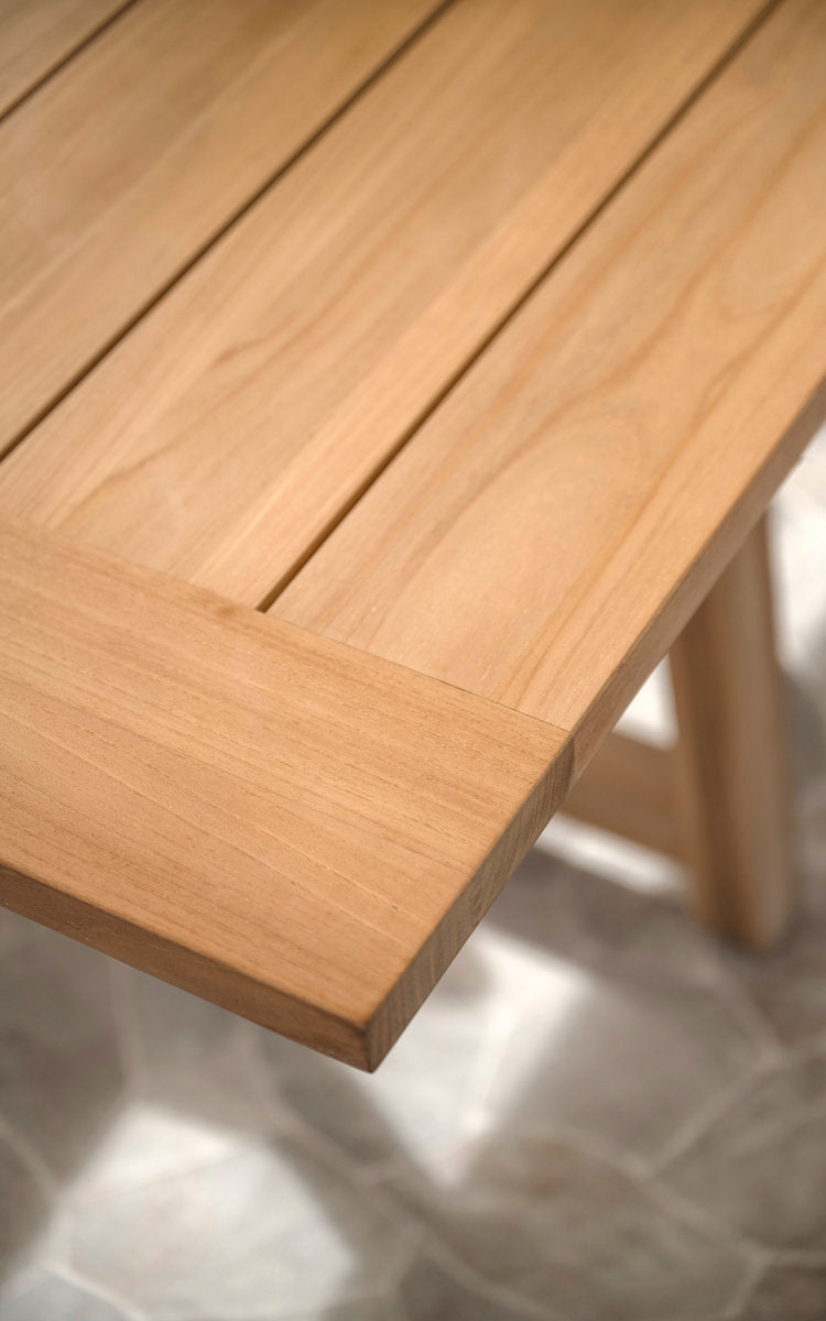 This is a close-up image of George Teak Extendable Table 200-280x100 cm in teak outdoor. Smooth teak tabletop edge and leg.