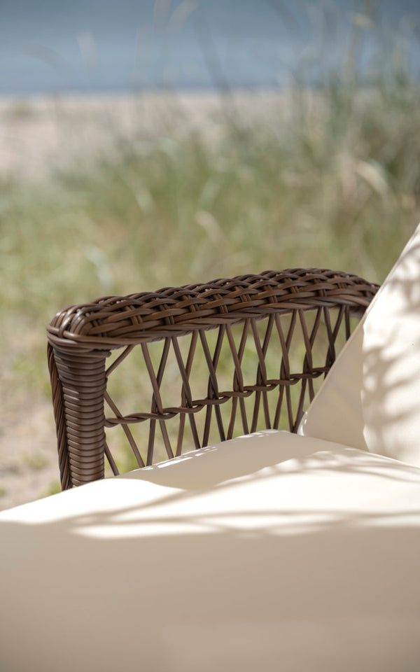 This is a close-up image of Daisy Exterior Sunbed in brown artfibre aluminum. Woven armrest with cream cushion.