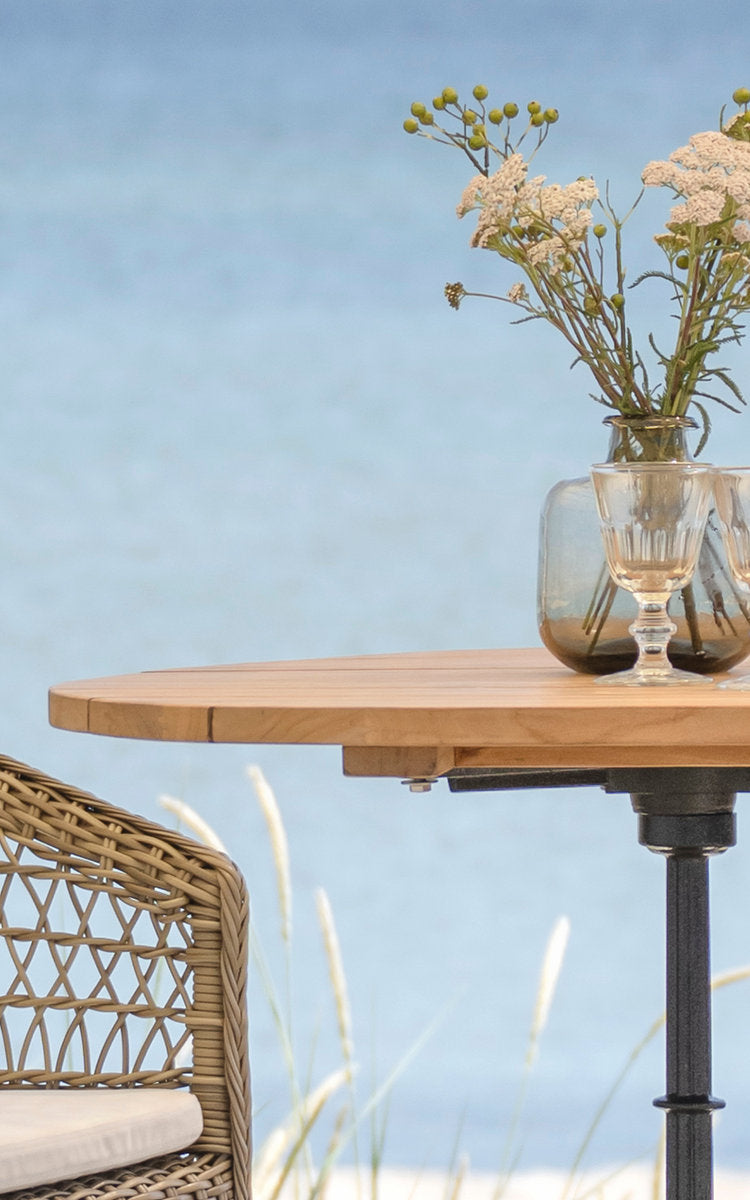 This is a close-up image of Lyon Bar Table-Teak Ø80 cm in cast iron. Round teak top on an iron base with flowers.