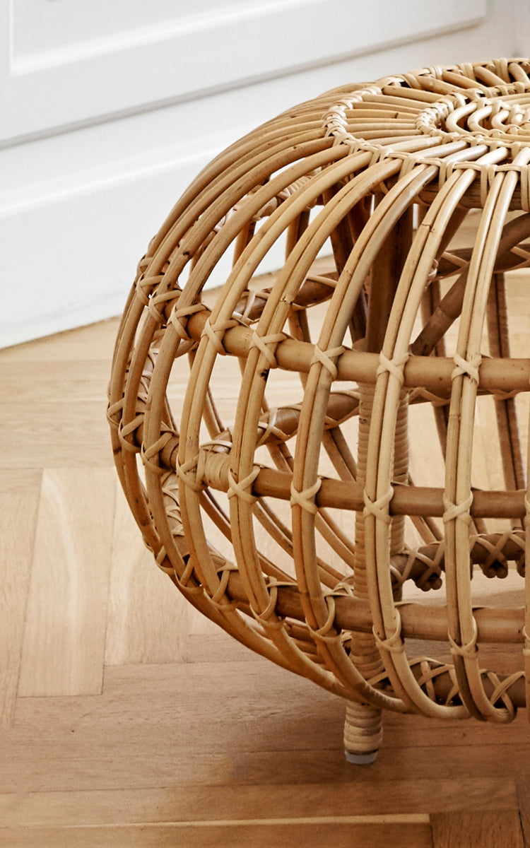 This is a close-up image of Ottoman Small in natural skin on rattan. Detail of the open rattan cage with curved ribs and cross bindings.